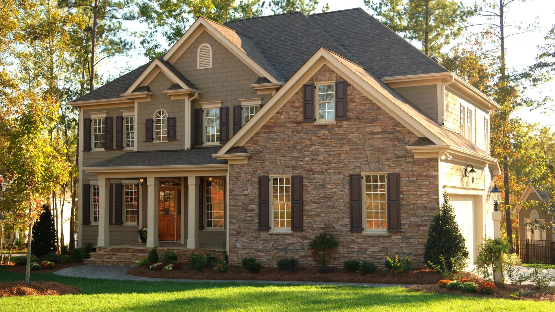 Two-story stone and siding house with dark shutters in wooded setting