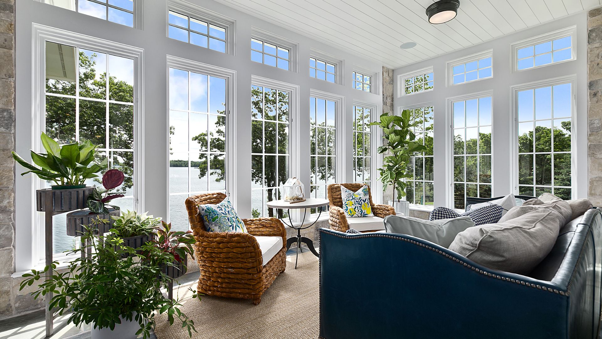 Bright sunroom with large windows, lake view, woven chairs, and indoor plants