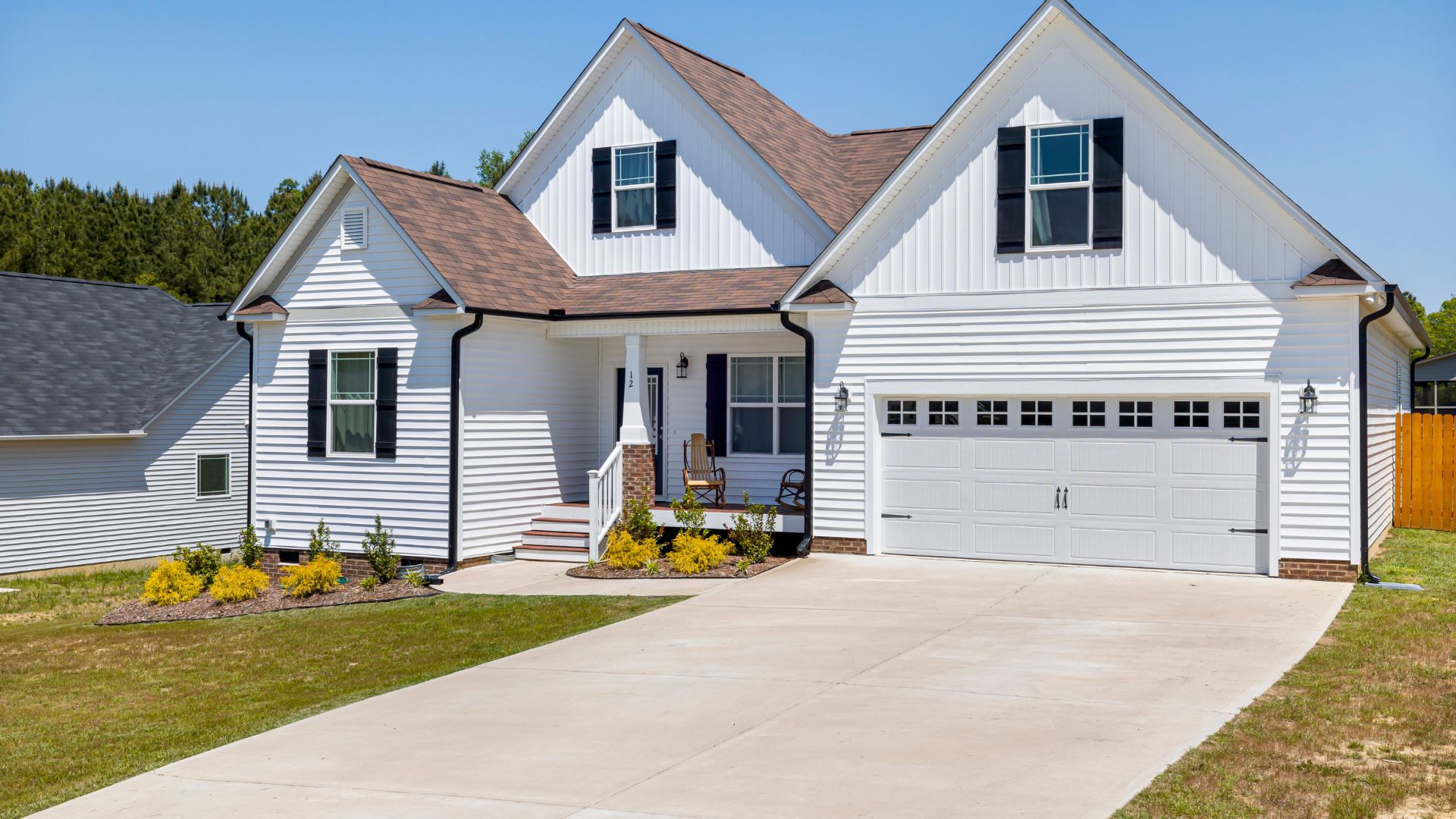 White two-story house with black shutters, garage, and yellow flower landscaping