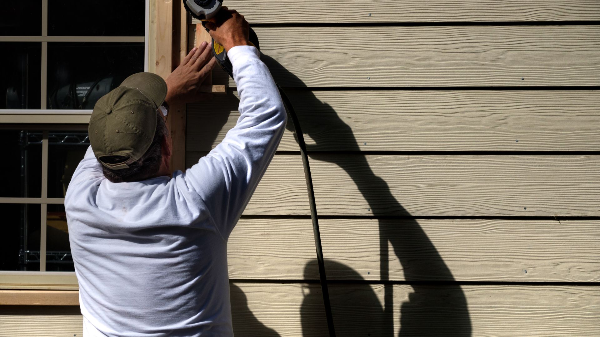 Worker installing siding on a house exterior with tools and shadow