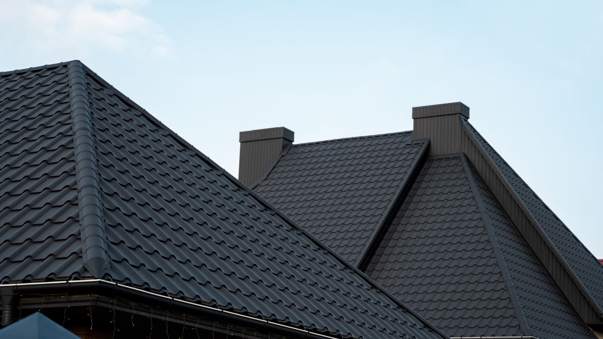 Dark gray tiled roof with multiple angles and two chimneys