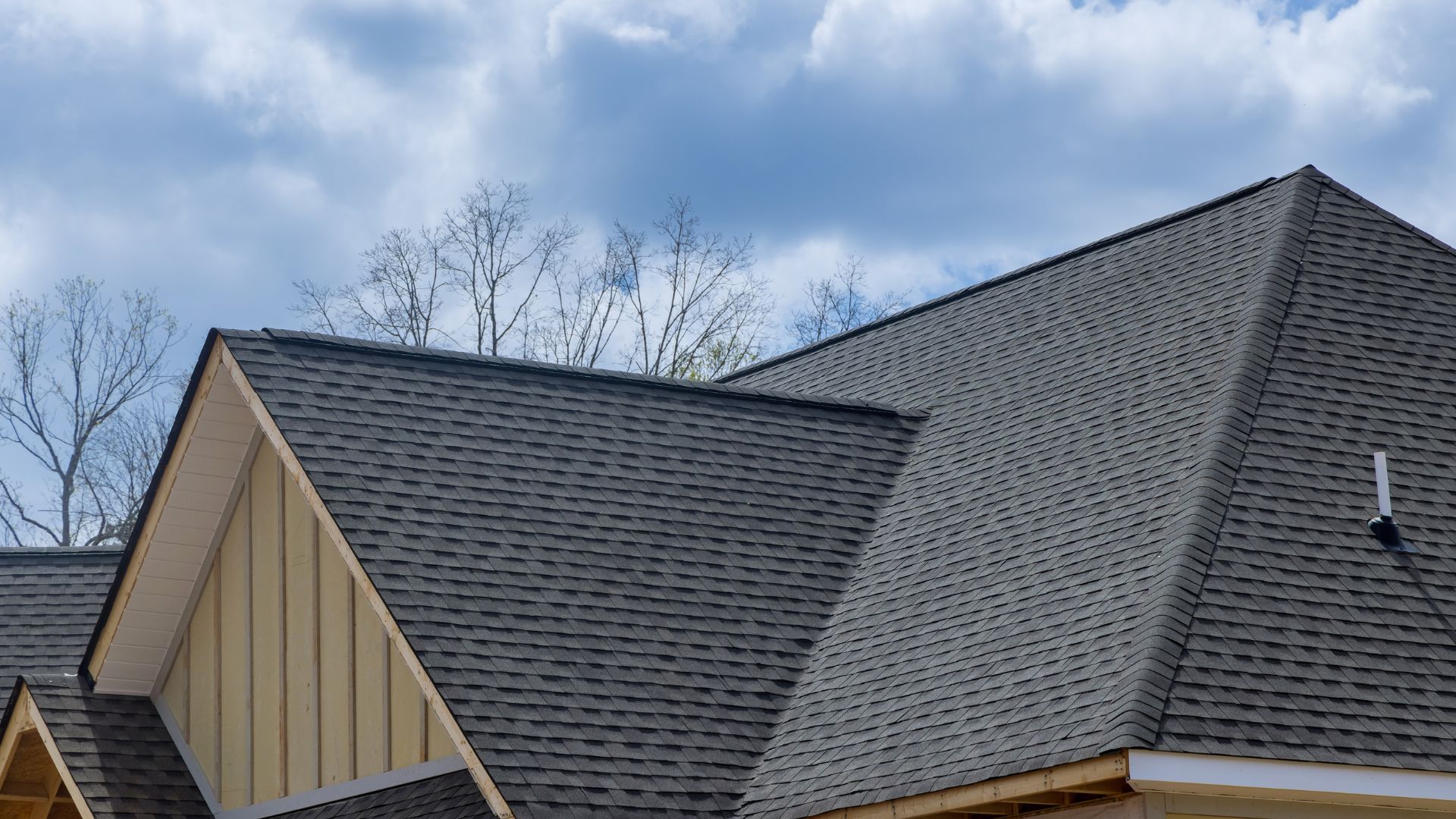 Gray shingle roof with complex angles against blue sky and bare trees
