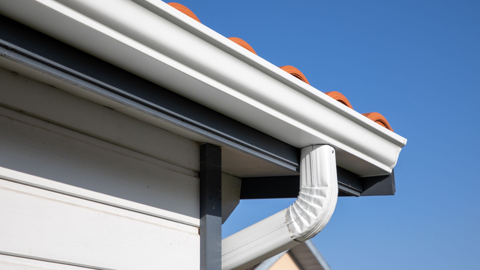 White gutter and downspout against blue sky and orange-topped roof