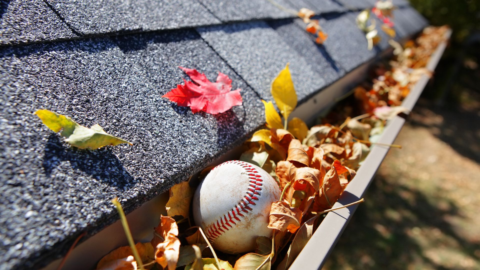 A homeowner cleaning leaves and debris out of a home's gutter system.