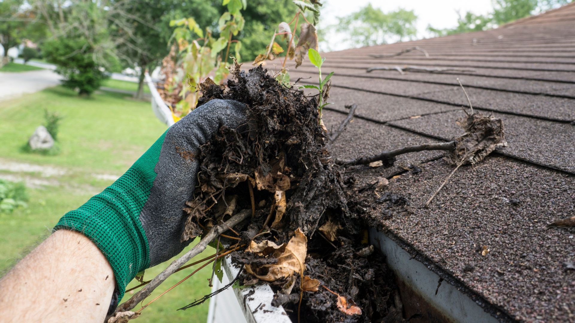 Gloved hand cleaning leaves and debris from roof gutter
