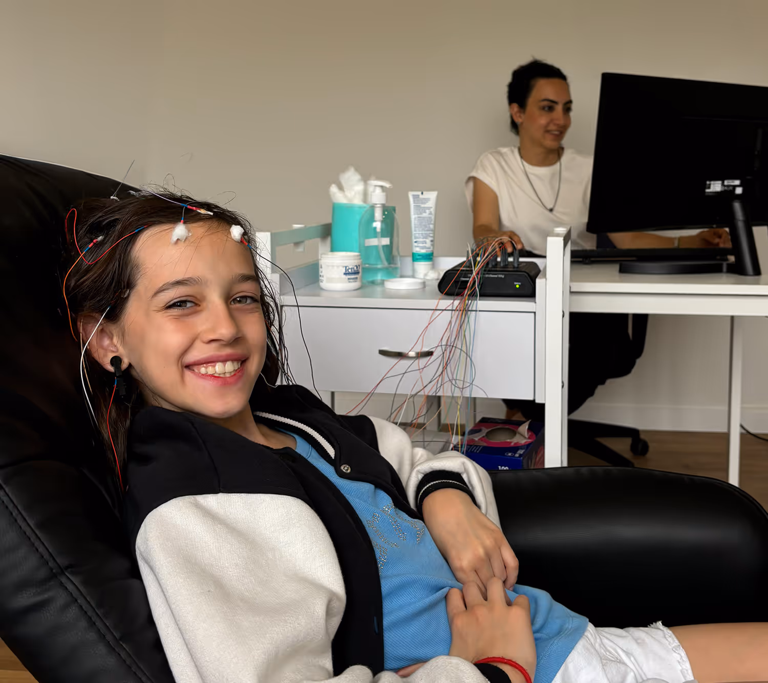 Criança sentada numa cadeira durante uma sessão de neurofeedback, com elétrodos colocados na cabeça, num ambiente clínico.