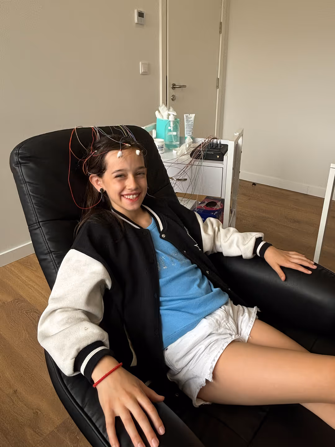 Criança sentada numa cadeira durante uma sessão de neurofeedback, com elétrodos colocados na cabeça, num ambiente clínico.
