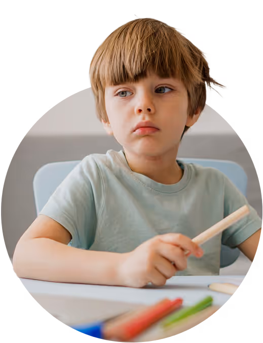 Criança sentada à secretária com materiais escolares, aparentando dificuldade de concentração durante uma atividade.