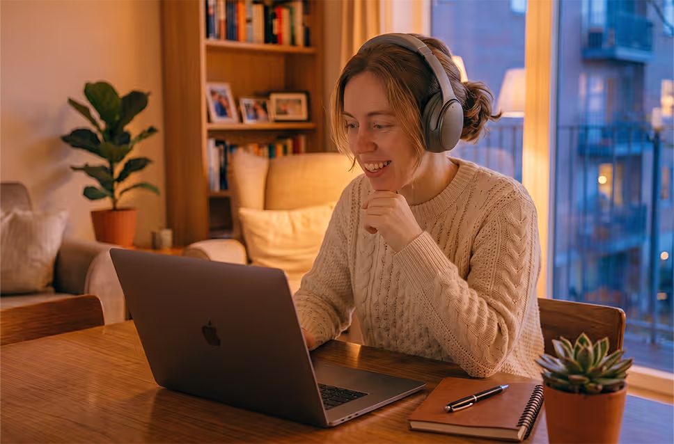Mulher a realizar uma formação online ao entardecer, com ar sorridente e auscultadores nos ouvidos