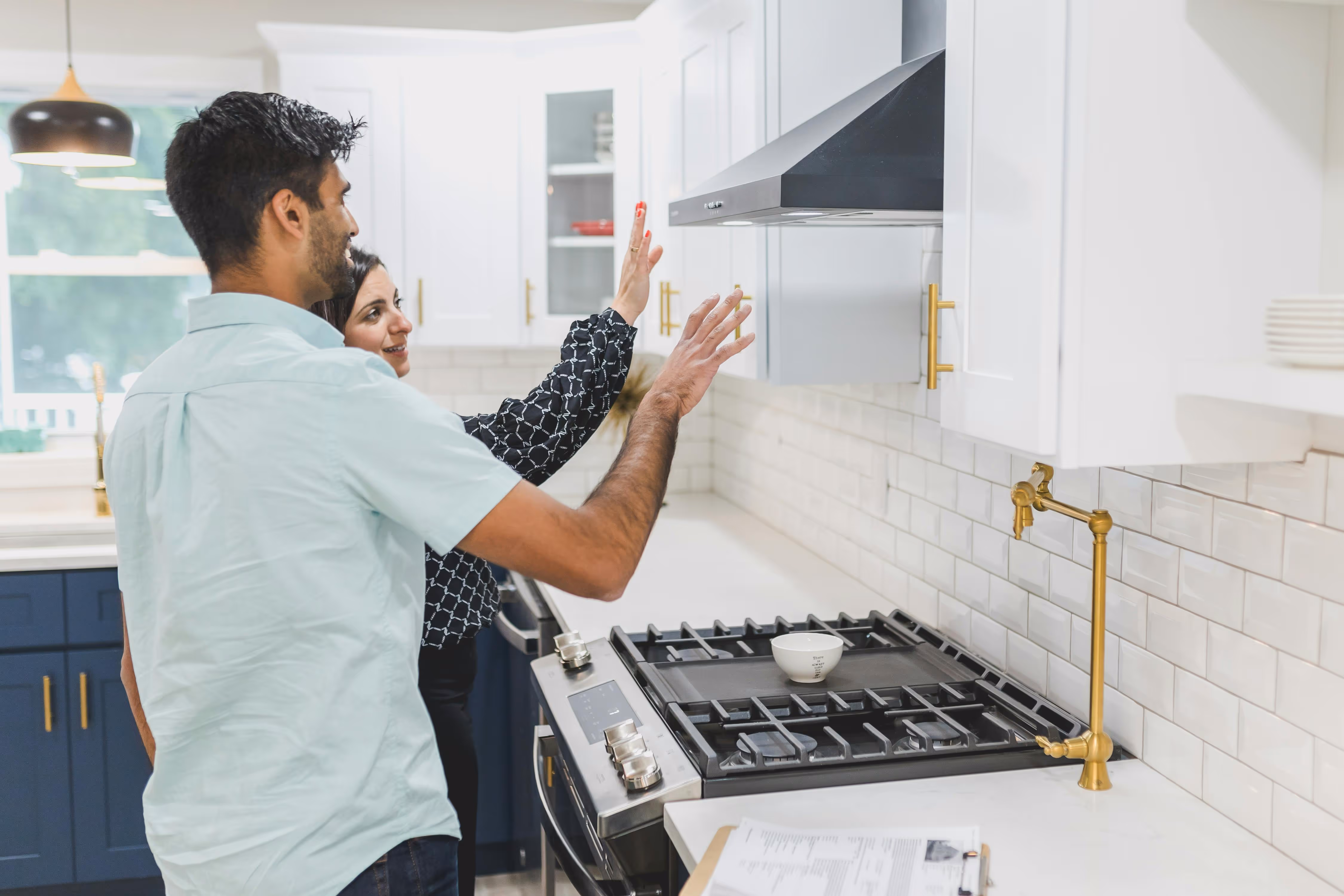 Man and woman examining and pointing at a modern kitchen stove and range hood in a bright kitchen.