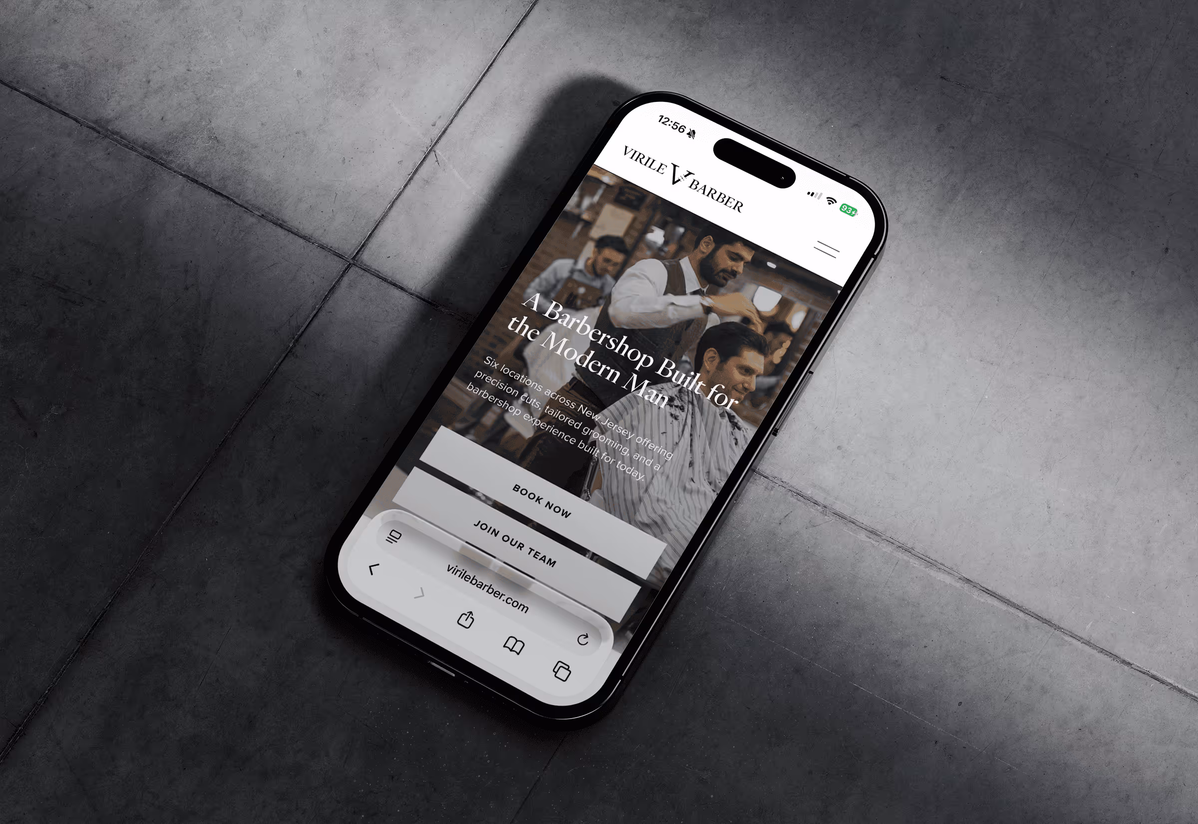 Smartphone displaying Virile Barber website featuring a barber cutting a man's hair with options to book now or join the team.