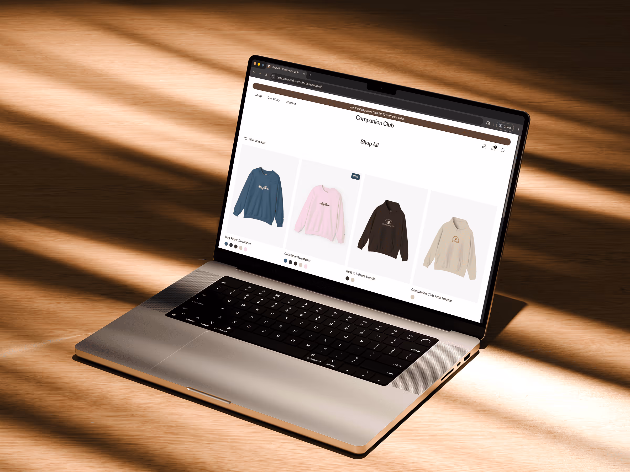 Laptop on wooden surface displaying an online store page with sweatshirts and hoodies for sale.
