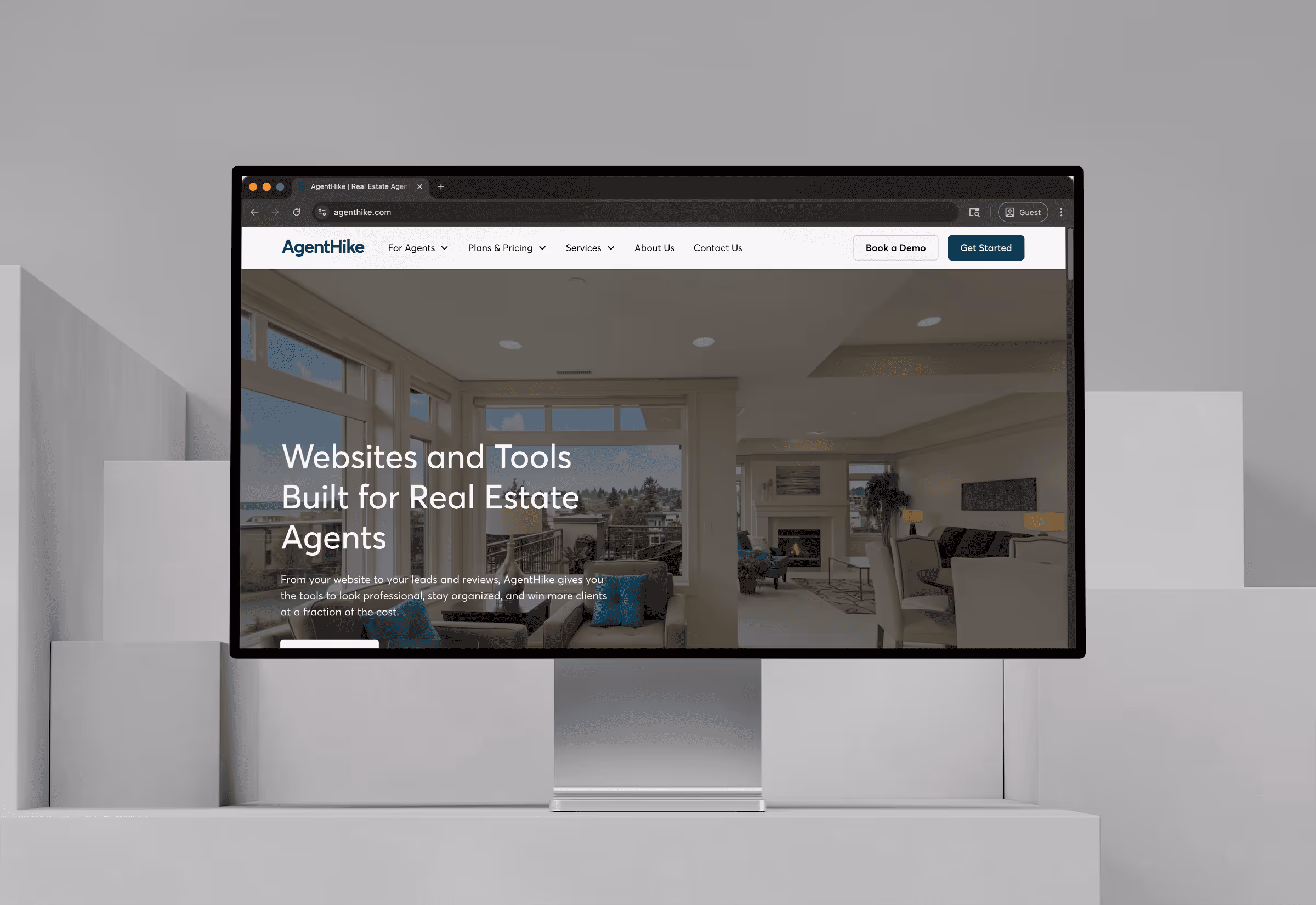 Computer monitor displaying AgentHike website homepage with text about websites and tools for real estate agents and a living room background.