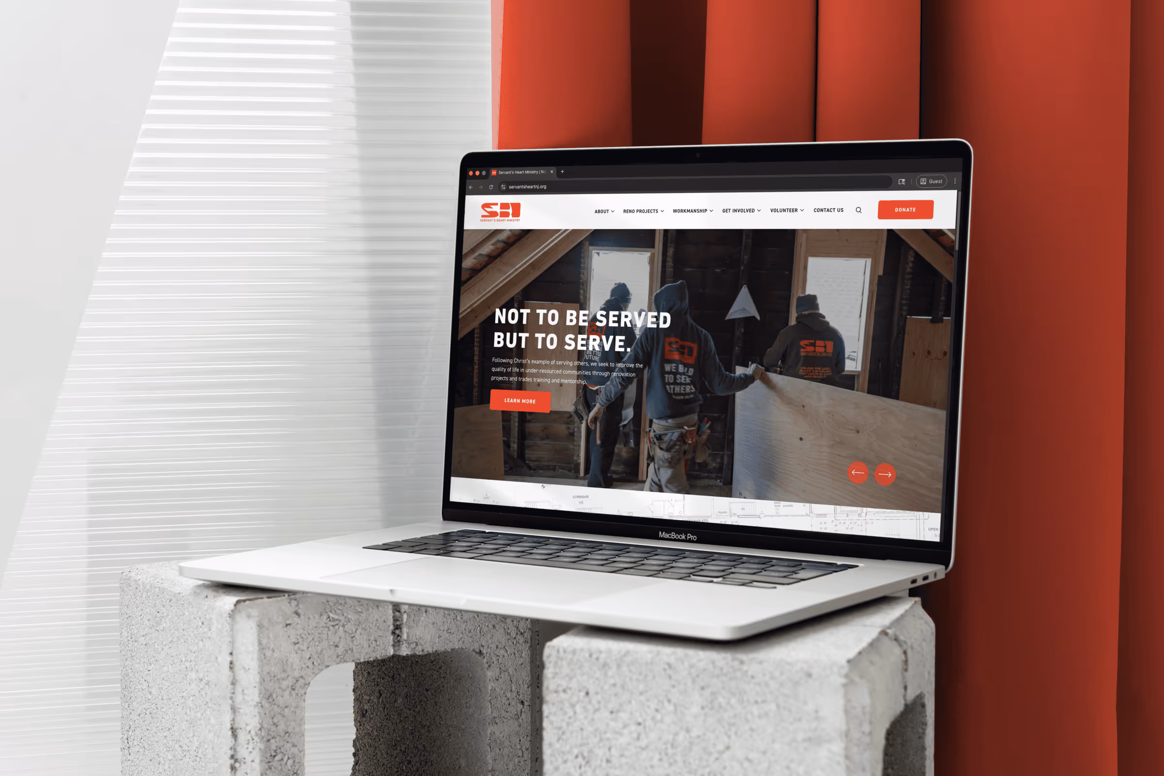 Open MacBook Pro displaying a website with workers holding plywood inside a construction site.