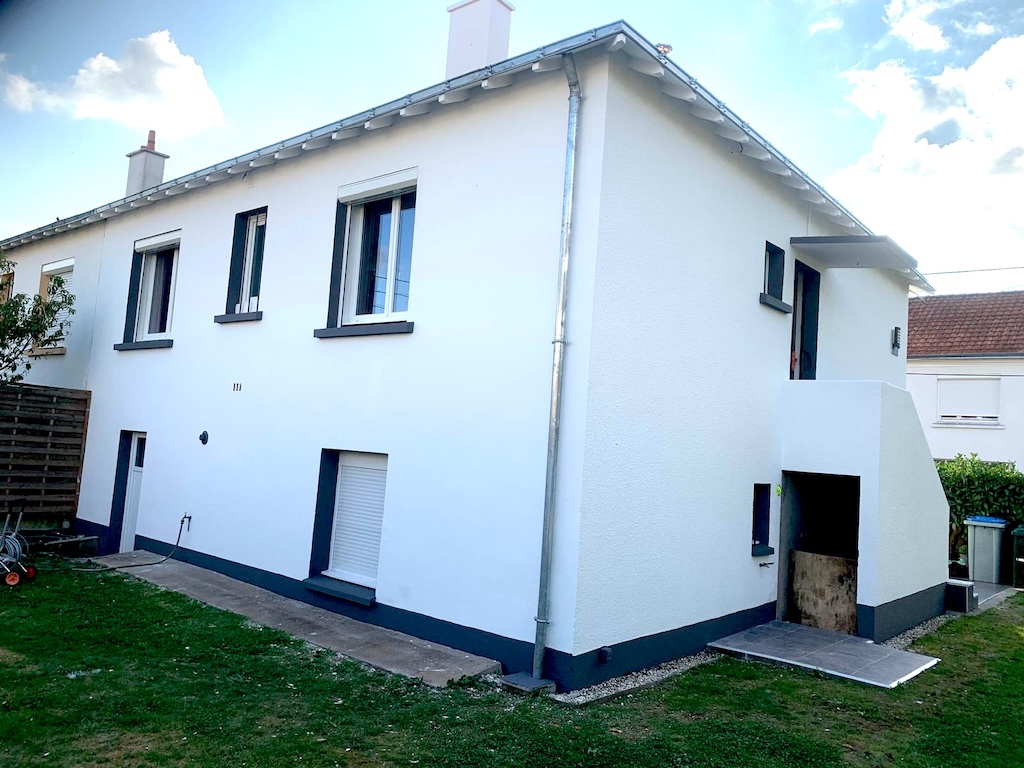Maison blanche avec plusieurs fenêtres, une porte, un petit escalier et une pelouse verte autour.