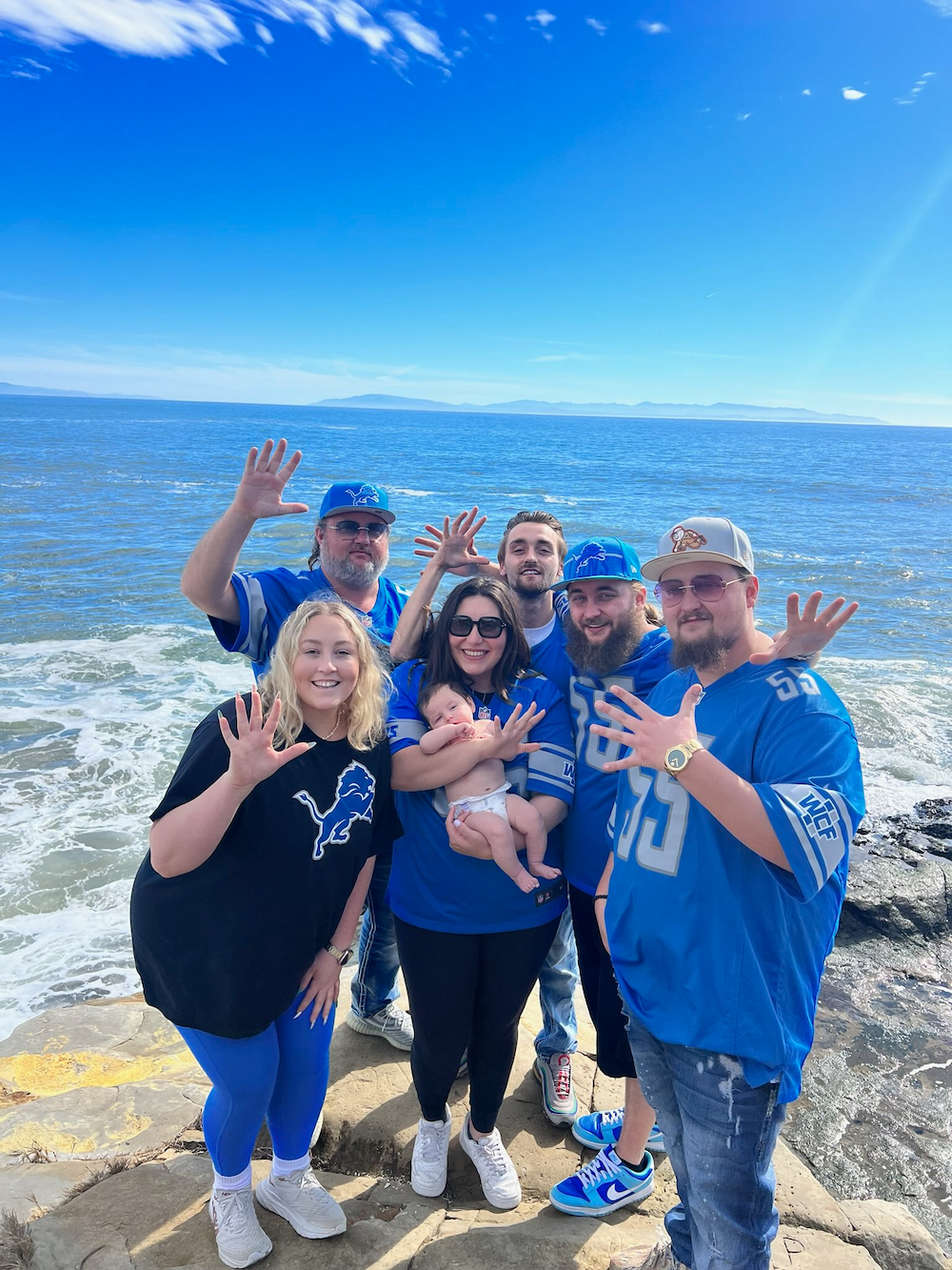 NIDIA Lions fans wave enthusiastically by ocean with baby, matching blue jerseys