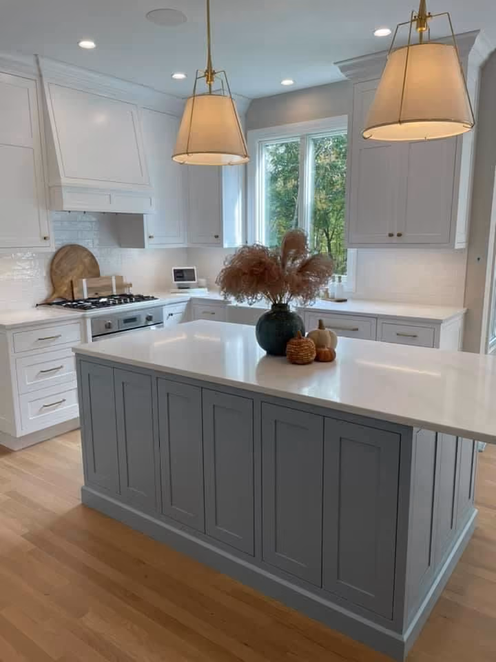 This may contain: a kitchen with white cabinets and an island in the middle of the room is lit by two pendant lights