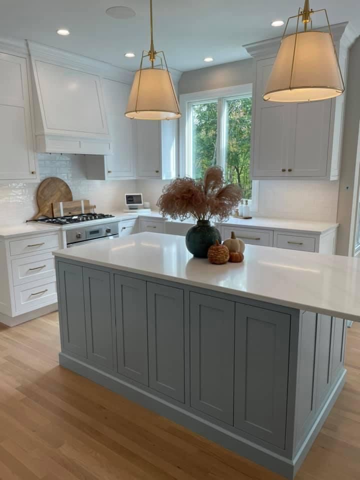 This may contain: a kitchen with white cabinets and an island in the middle of the room is lit by two pendant lights