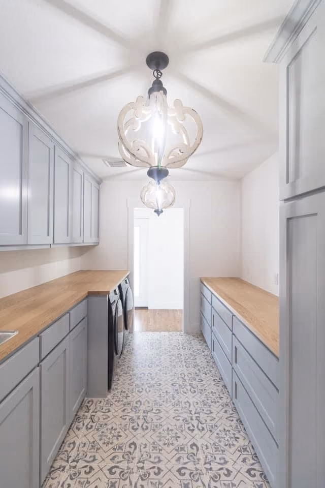 This may contain: an empty kitchen with grey cabinets and white walls, light fixture in the middle is hanging from the ceiling
