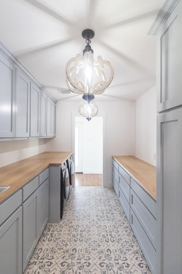 This may contain: an empty kitchen with grey cabinets and white walls, light fixture in the middle is hanging from the ceiling