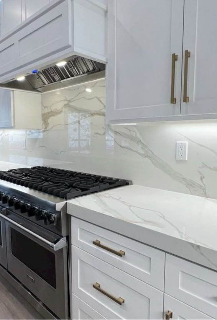 This may contain: a kitchen with white cabinets and marble counter tops, an oven and stove top in the middle