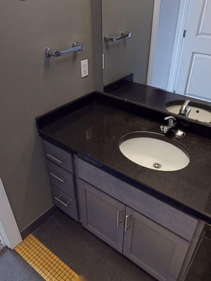 This may contain: a bathroom with a black counter top and white sink under a mirror next to a door