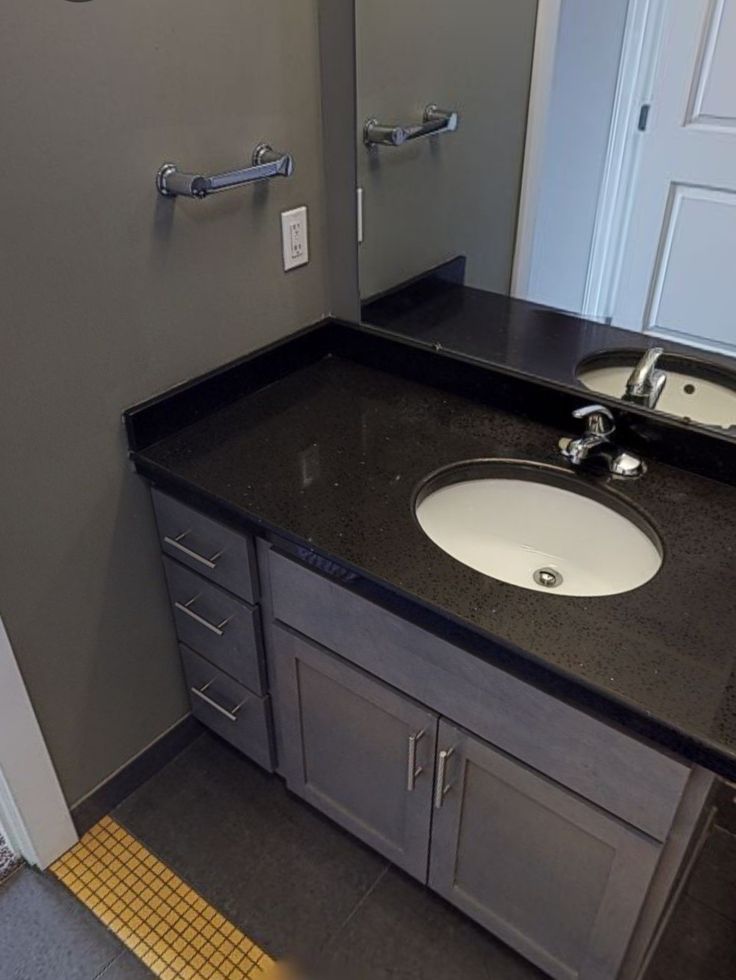 This may contain: a bathroom with a black counter top and white sink under a mirror next to a door