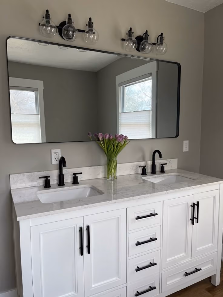 This may contain: a bathroom vanity with two sinks and a large mirror above it, in front of a window
