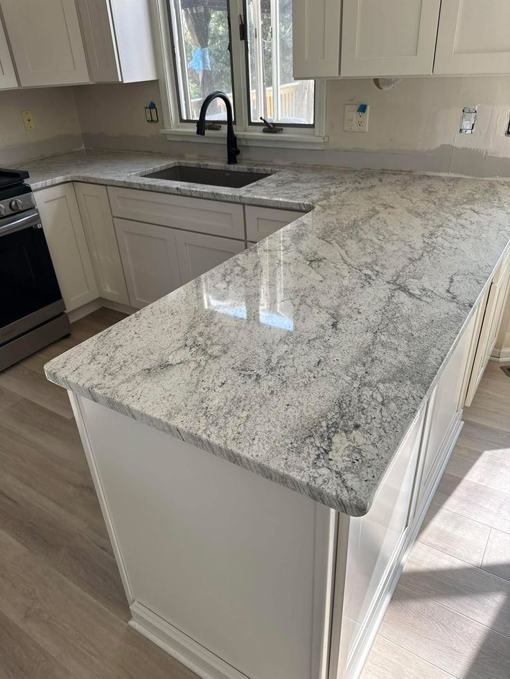 This may contain: a kitchen with white cabinets and granite counter tops in it's center island area