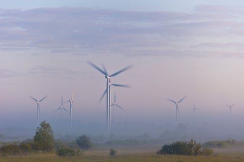 The blades of wind turbines emerge from the mist in rural Poland