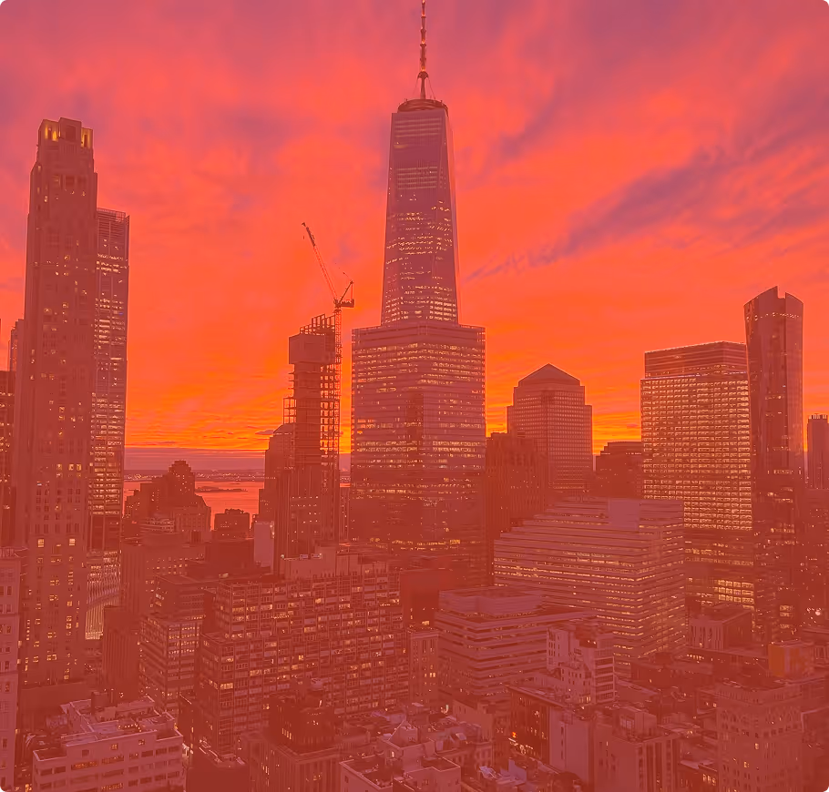 City skyline at sunset with tall buildings and an orange-red sky.