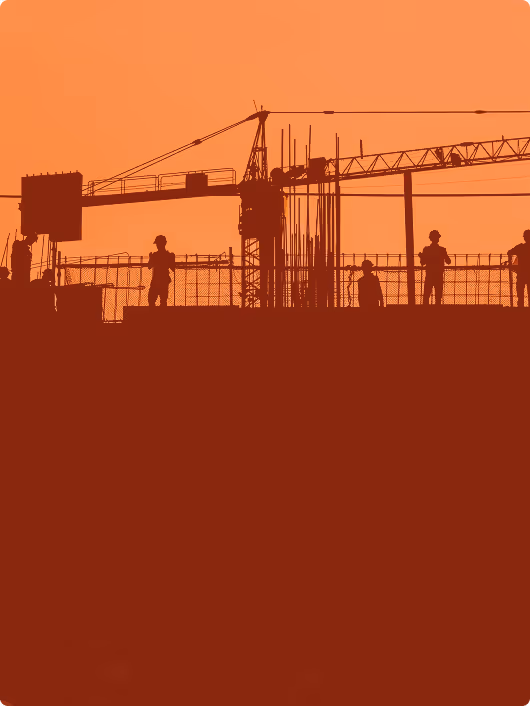 Silhouettes of construction workers on a building site with cranes in the background against an orange sky.