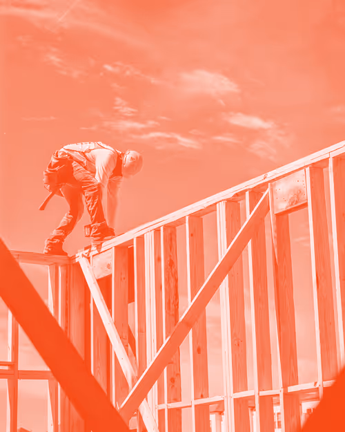 Construction worker standing on a wooden frame structure under a partly cloudy sky, tinted in red.
