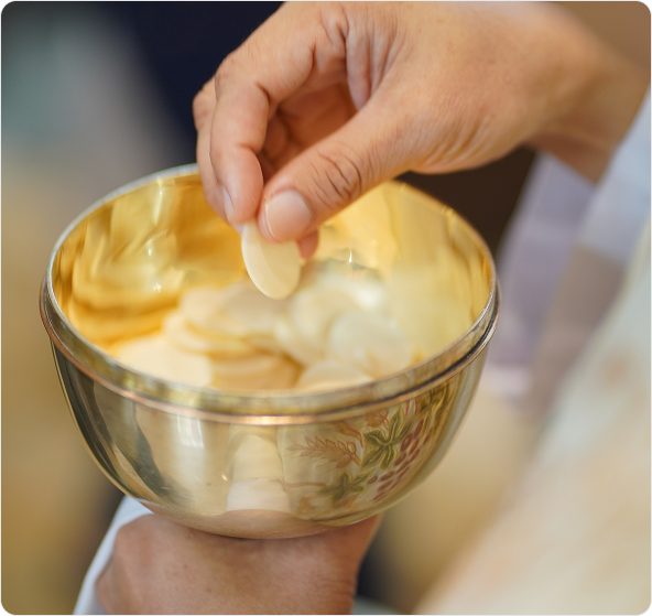 A hand holding a host over a chalice during a religious ceremony.