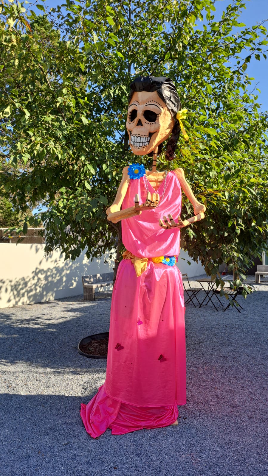 Catrina decorativa de pie frente a unos árboles.
