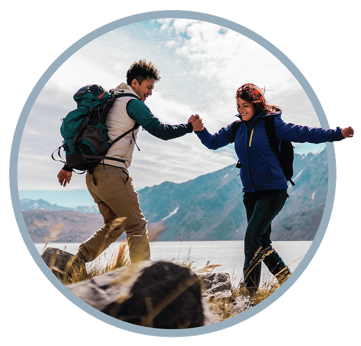 Two hikers holding hands and smiling with mountains and lake in the background.