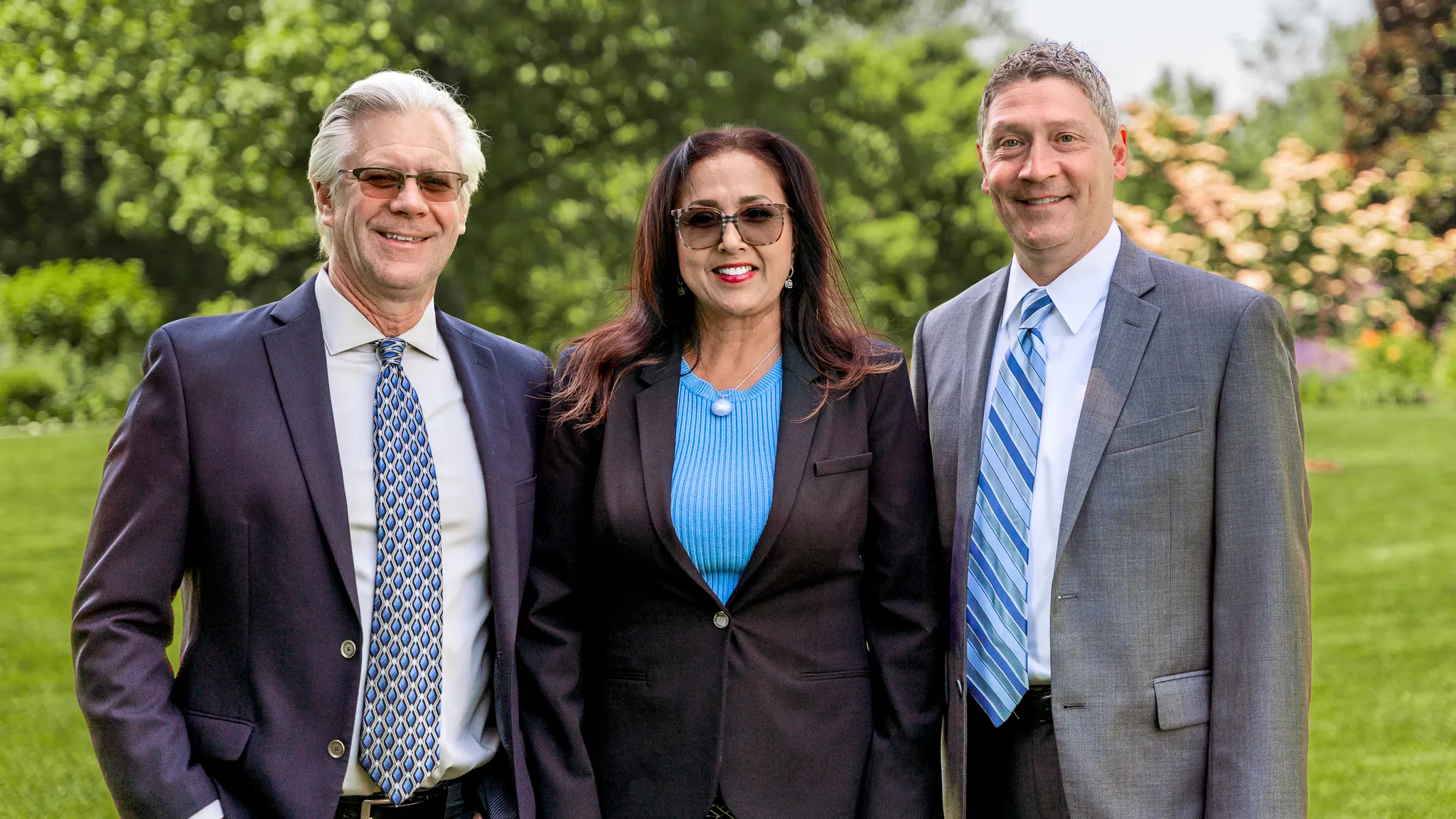 Three Snider Financial Group advisors in business attire standing outdoors with green trees and grass in background.