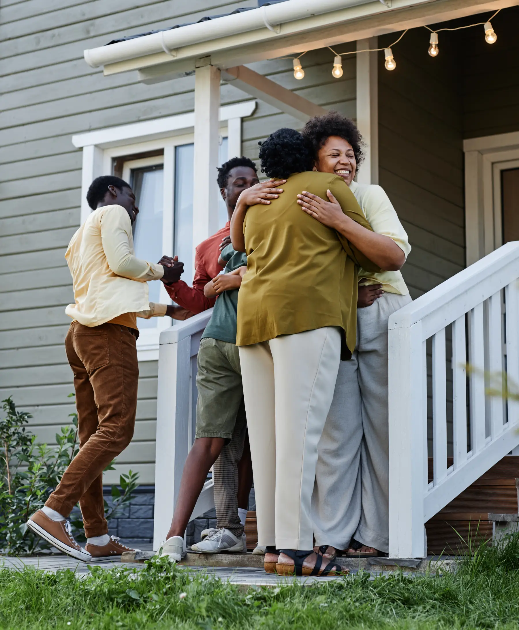 Family members greeting each other with a hug on the front porch of a home.