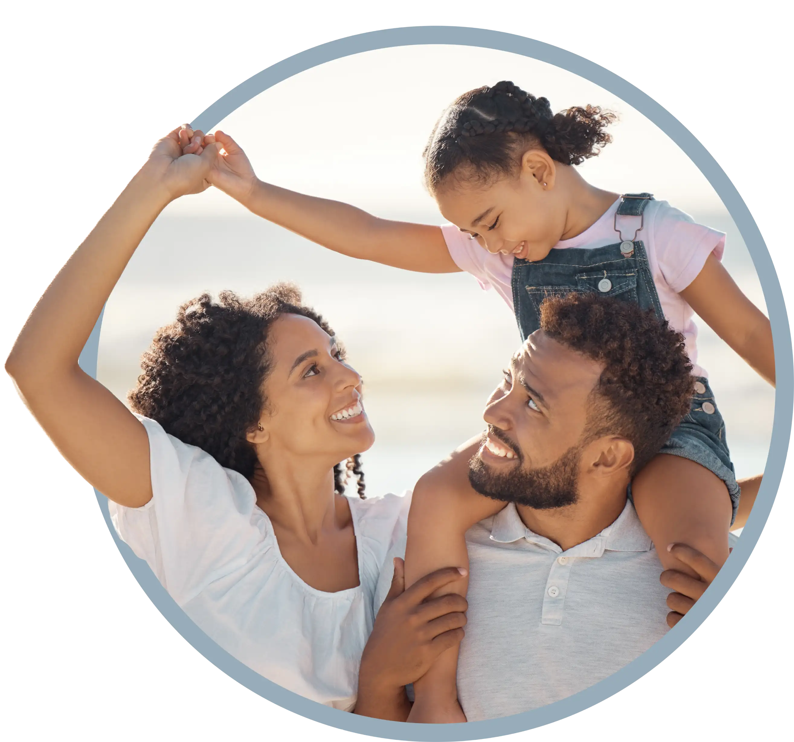Smiling family with child on father's shoulders holding hands with mother outdoors.