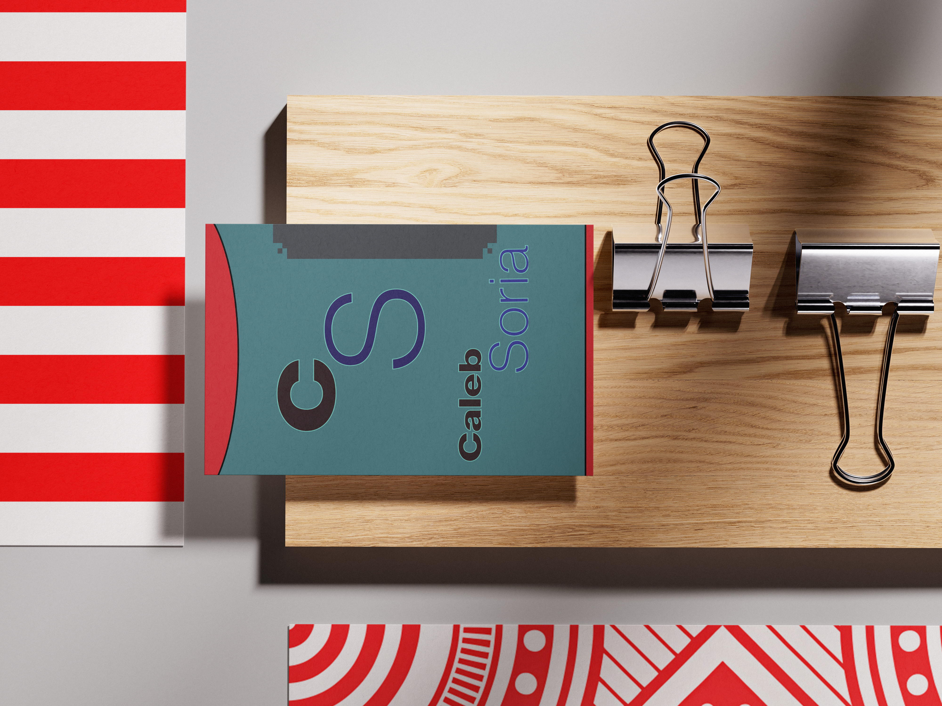 Business card with 'Caleb Soria' and stylized letters 'CS' on a wooden surface next to two metal binder clips.