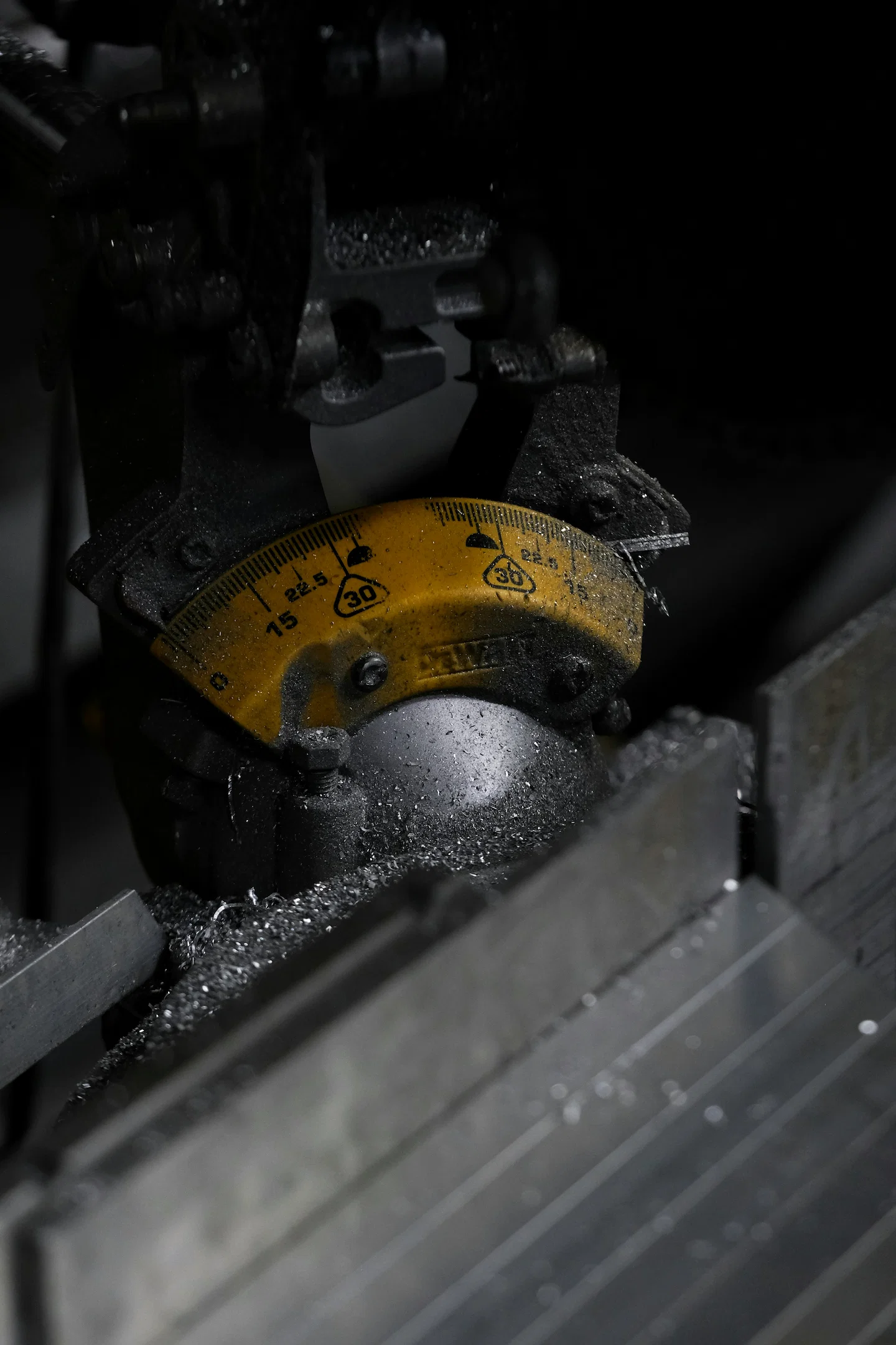 Close-up of an industrial CNC cutting machine showing a yellow angle gauge and metal blade surrounded by metal shavings during a precision cutting process.