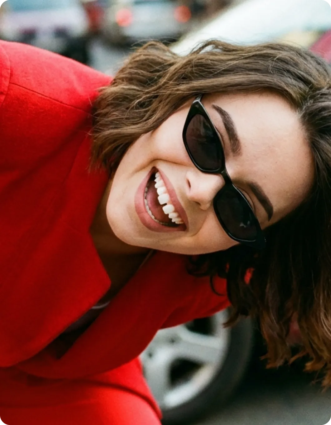 A woman in a red jacket and sunglasses smiling.