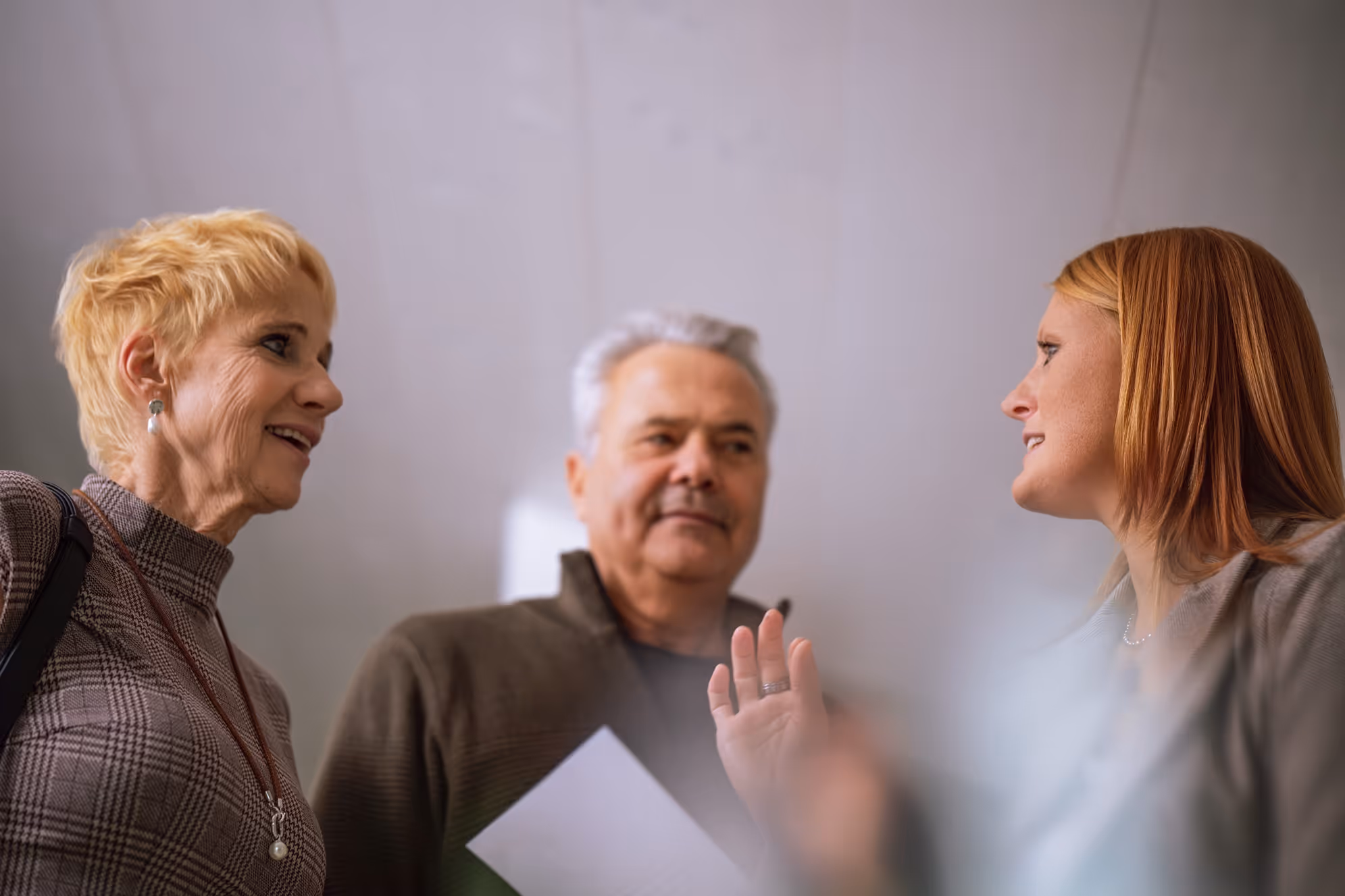 Drei Erwachsene unterhalten sich, einer hält ein Papier in der Hand, eine andere gestikuliert mit der Hand.