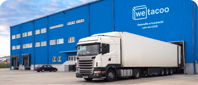 White semi-truck parked at loading dock of blue warehouse with WeTacoo logo and slogan in Italian.