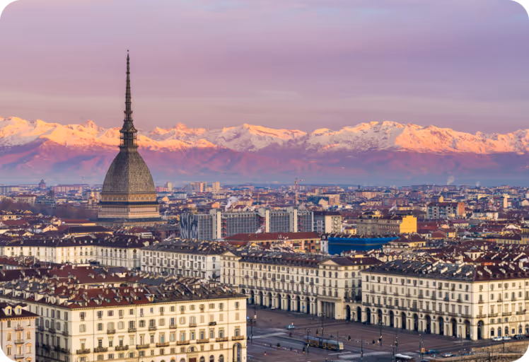 View of Turin city with the Mole Antonelliana tower and snow-capped Alps glowing pink at sunset.
