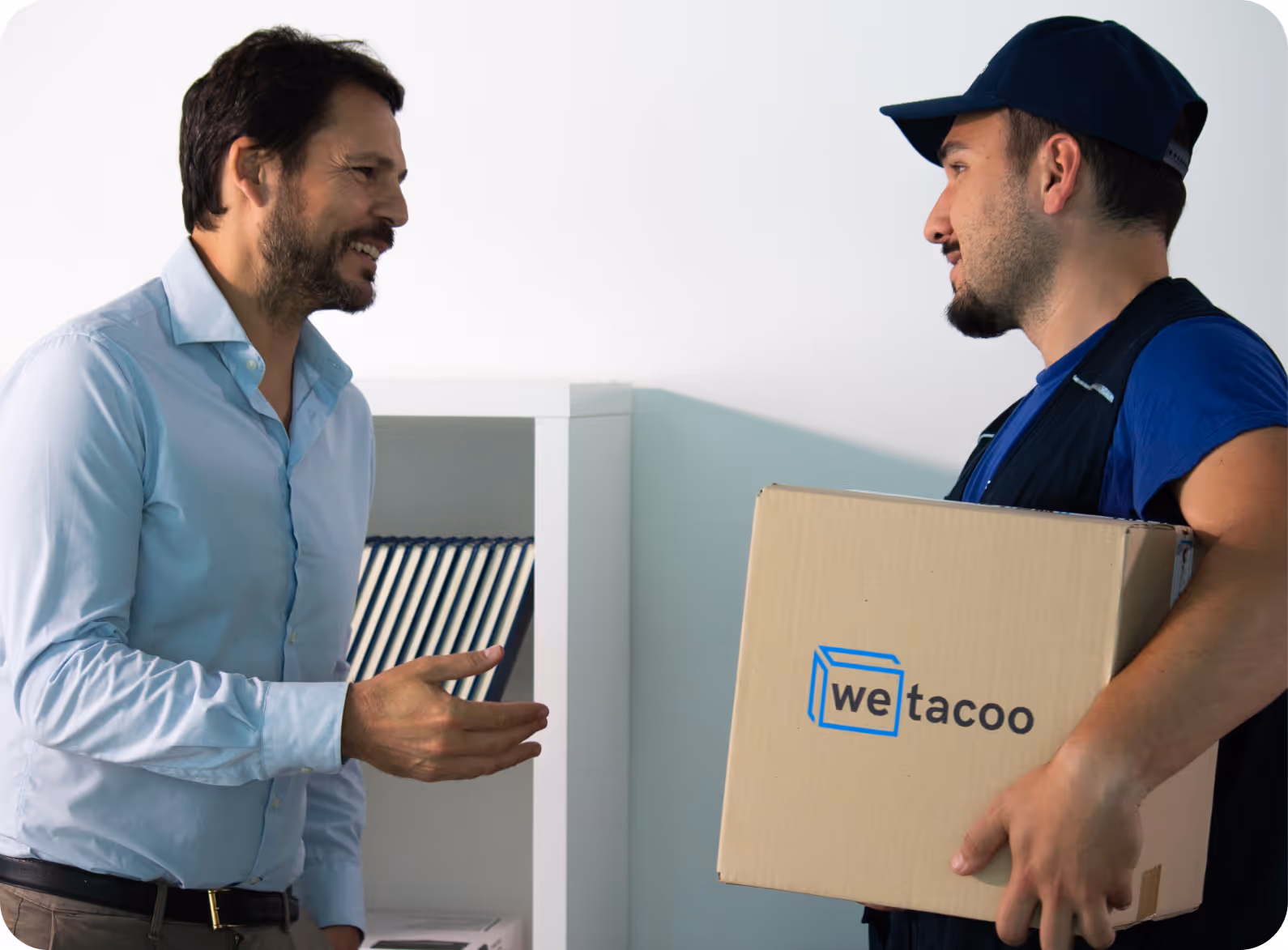 Man in light blue shirt talking to delivery worker holding a box labeled 'wetacoo' inside an office.