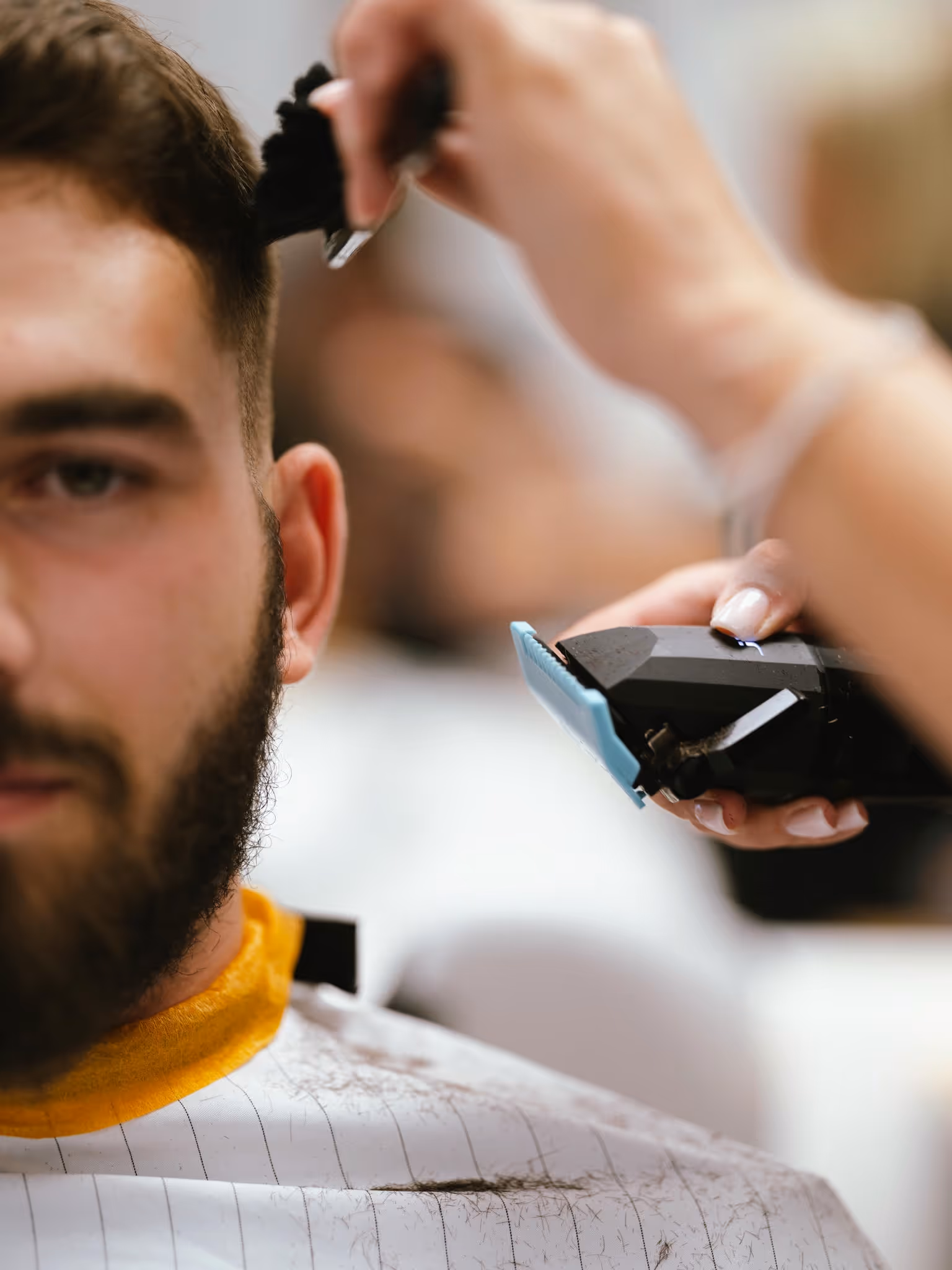 A man getting a bear trim by a woman with beard clippers