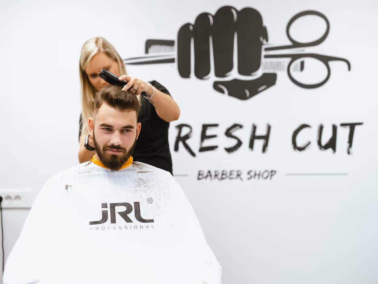 Tina the barbershop owner cutting a hair of a young male that sits in a barbershop chair