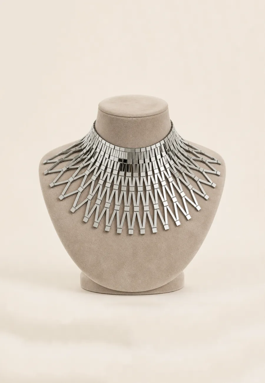 Collier géométrique argenté présenté sur un buste beige.