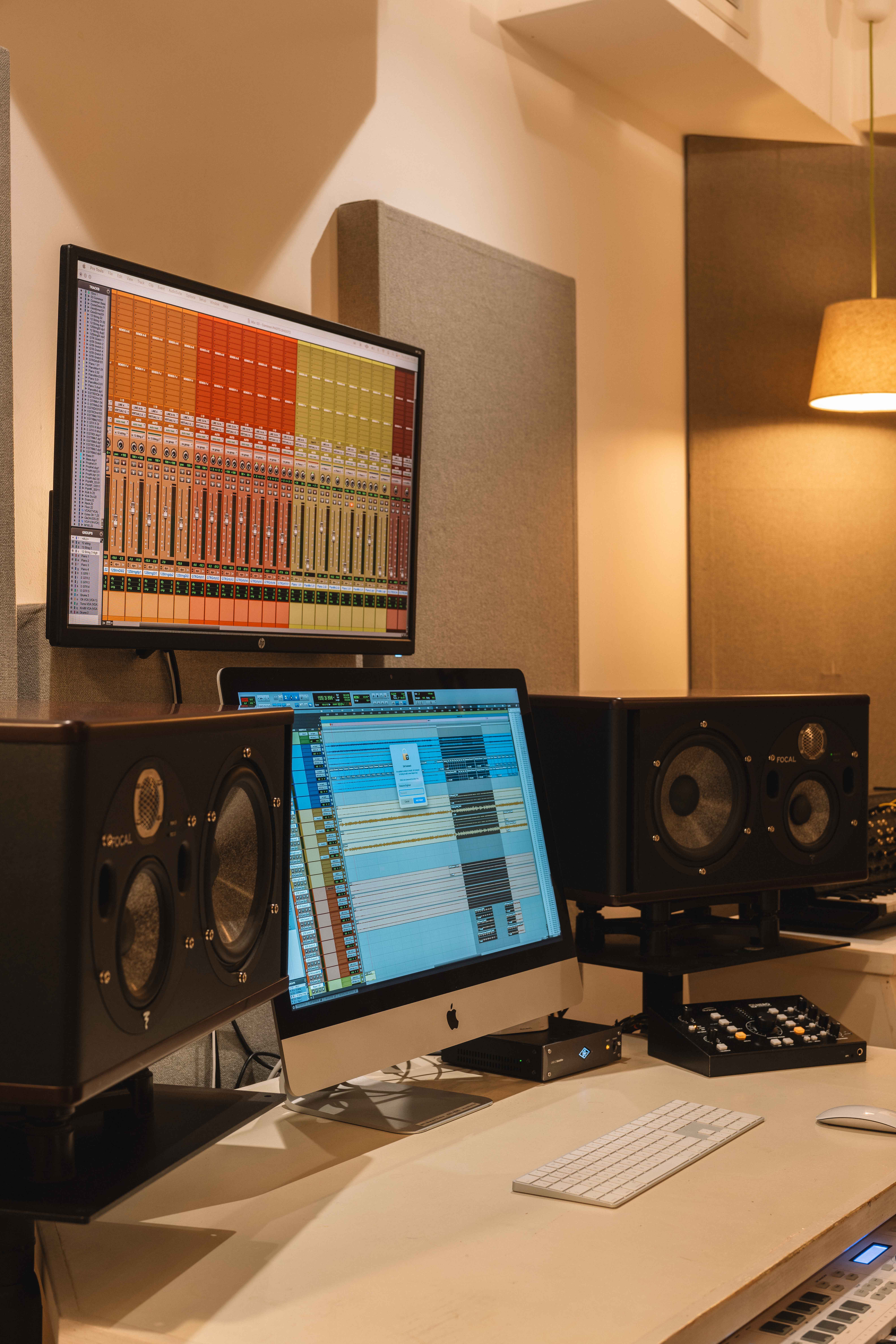Music production studio with dual monitors displaying digital audio workstation software and black Focal studio speakers on each side.